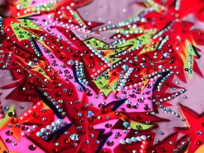 Detalle de una prenda de gimnasia con pedrería sobre estampado rojo y fucsia