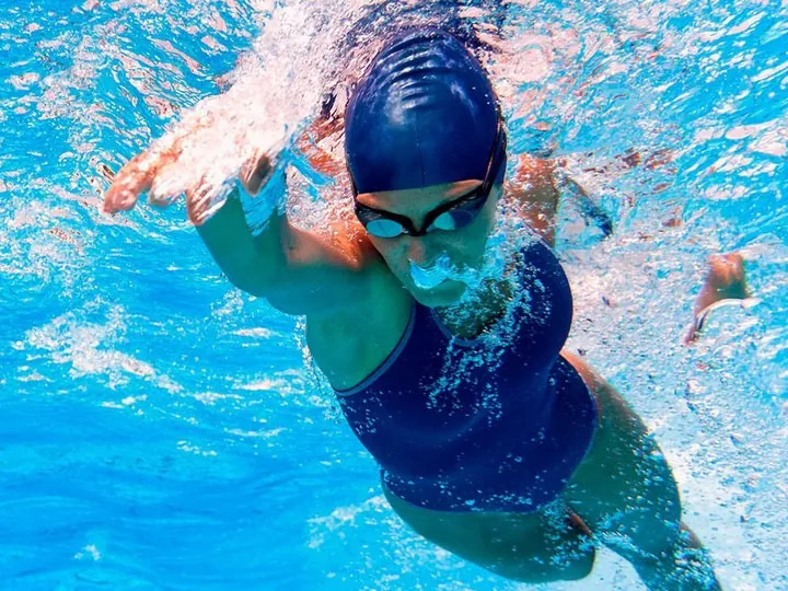 Nadadora con gorro y traje de baño azul nadando estilo libre